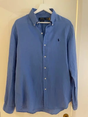 Ljusblå linneskjorta från Polo Ralph Lauren - Säljer en klassisk blå skjorta i linne från Polo Ralph Lauren med custom fit strl M. Perfekt för en clean och stilren look.