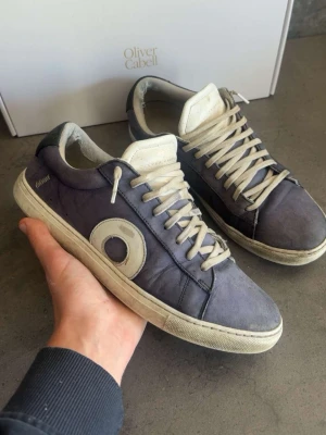 Lila sneakers från Oliver Cabell - Snygga lila sneakers från Oliver Cabell med vit sula och vita detaljer. Skorna har en rundad tå, vita skosnören och en stor vit cirkeldetalj på sidan. Ovandelen är i mocka och insidan är fodrad i textil. Perfekta för en cool och avslappnad stil.