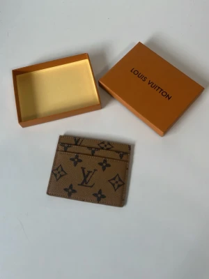 L och V brun kortfodral - Snyggt brunt kortfodral från L och V med klassiskt monogrammönster i mörkbrunt. Tillverkat i tåligt läder med flera kortfack. Perfekt för dig som vill ha en stilren och lyxig accessoar i fickan.