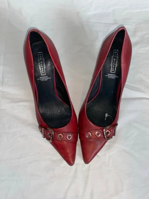 Nya burgundy spetsiga klackar från 5TH Avenue  - Skit snygga trendiga vinröda pumps i äkta läder! Spetsig tå med coola spännen som detaljer. Klackarna är ifrån "5th avenue".  Aldrig använda, endast testade. Men säljer pga att de tyvärr är förstora. Klacken är smal och elegant, och insidan är svart. Perfekta för dig som vill ha en edgy men stilren look!! Storlek 38. (Nypris 1000kr/ 99euro) 