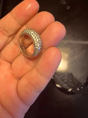Silverring från Smycka  - Kupolformad ring (bombe-modell) i äkta 925 Sterling silver. Ovansidan är helt täckt av tätt glittrande, pavéinfattade stenar.  Ringen är köpt på Smycka och är tillverkad av det svenska kvalitetsmärket Tångring925. Den har mycket tydliga äkthetsstämplar på insidan av skenan: ”925” (äkta silver), ”TR” (Tångring925) samt den officiella kontrollstämpeln. - Material: Äkta 925 Sterling silver & cubic zirconia Obs! Se bilder för mått då jag är osäker på storleken. 