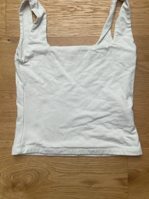 Vit topp  från Gina Tricot - Säljer en enkel och stilren vit linnetopp från Gina Tricot. Toppen har breda axelband och rak skärning, perfekt att matcha med jeans eller kjol. Materialet känns mjukt och bekvämt mot huden.