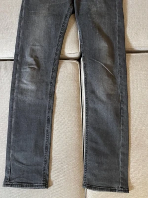 Grå raka jeans från Lee - Säljer ett par grå jeans från Lee med raka ben och knappgylf. Jeansen har klassisk femficksdesign och är tillverkade i ett mjukt denimtyg. Perfekta för en avslappnad och stilren look.