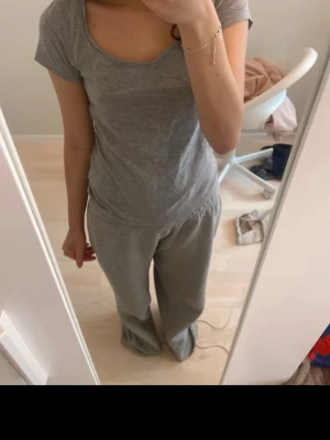 Grått loungewear-set med t-shirt - Mysigt loungewear-set i mjukt grått tyg. Setet består av en enkel t-shirt med rund halsringning och korta ärmar samt ett par lösa byxor med resår i midjan. Perfekt för chill dagar hemma eller när du vill vara bekväm.