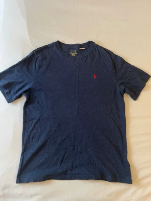 Mörkblå t-shirt från Polo Ralph Lauren - Klassisk mörkblå t-shirt från Polo Ralph Lauren med rund hals och korta ärmar. Liten röd broderad logga på bröstet ger en stilren touch. Tillverkad i mjuk bomull för skön känsla hela dagen.