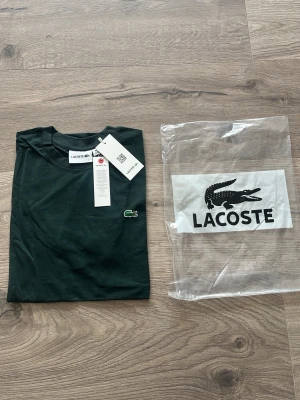 Mörkgrön Lacoste t-shirt i bomull - Snygg mörkgrön t-shirt från Lacoste med klassisk krokodillogga på bröstet. Tillverkad i mjuk bomull och har en enkel, stilren design med rund hals och korta ärmar. Perfekt för en clean och avslappnad look.