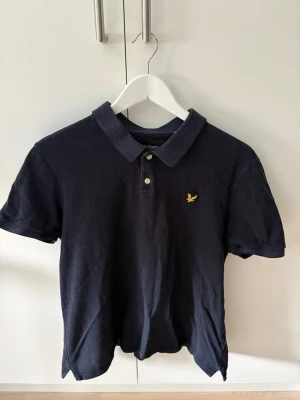 Mörkblå piké från Lyle & Scott  - Snygg mörkblå pikétröja från Lyle & Scott med klassisk krage och två knappar framtill. Pikén passar XL. L och till och med M. En klassiker som passar till allt! 