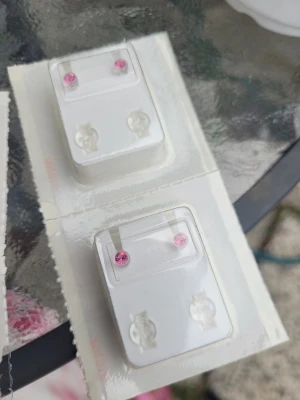 Rosa stiftörhängen med sten - Säljer två par små stiftörhängen med rund, rosa sten. Örhängena har en enkel och stilren design som passar perfekt till dig som gillar färg och diskreta smycken. Materialet ser ut att vara metall med glittrande rosa stenar framtill.