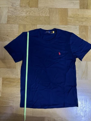 Mörkblå t-shirt från Polo Ralph Lauren - Snygg mörkblå t-shirt från Polo Ralph Lauren med klassisk röd logga broderad på bröstet. T-shirten har rund halsringning och korta ärmar. Tillverkad i mjuk bomull för en bekväm känsla. Perfekt till jeans eller shorts.