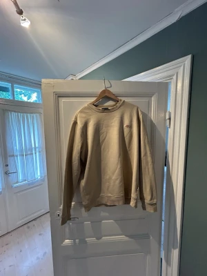 Beige sweatshirt från Dickies - Säljer en beige sweatshirt från Dickies med rund halsringning och liten logga på bröstet. Tröjan har en avslappnad passform, ribbade muddar vid ärmslut och nederkant. Perfekt för en chill och stilren look. Knappt andvänd 