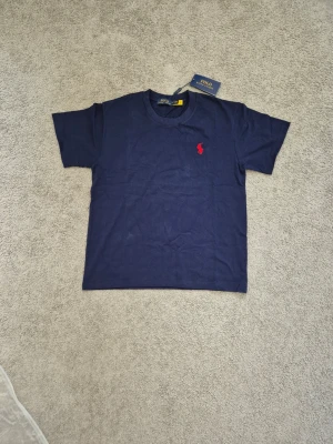 Polo Ralph Lauren - Snygg mörkblå t-shirt från Polo Ralph Lauren med klassisk vit logga broderad på bröstet. T-shirten har rund halsringning och korta ärmar. Tillverkad i mjuk bomull för en skön känsla och stilren look.