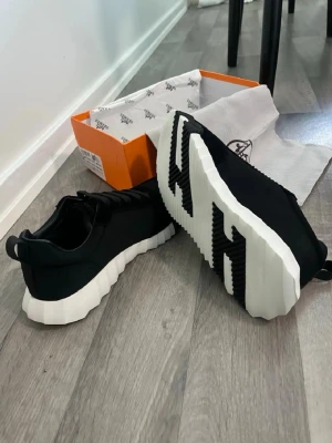 Hms skor - Svarta sneakers med chunky, räfflad vit sula och svarta skosnören. Ovandelen är i slätt material med detaljer i mockaliknande tyg. Sulan har en unik design med svarta inslag undertill. Perfekt för dig som gillar en modern och edgy stil.