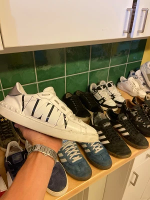 Vita Valentino Garavani sneakers - Säljer ett par vita sneakers från Valentino Garavani med stor VLTN-logga på sidan. Skorna har en chunky sula, nitar på hälen och är gjorda i läder. Snygg och modern design som sticker ut med sin grafiska logga och detaljer.