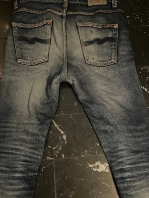 Nudie Lean Dean - Märke & Modell: Nudie, Lean Dean Storlek: W30 L32 (Passar S/M) Passform: Slim Skick: 6,5/10 Om plagget: Ikoniska Lean Deans i indigo med orange stitching och asfeta mörkblå bakfickor. Lagats i skrevet och vid låren av Nudie, slitage runt knän och högra bakfickan. Info: 100% äkta | Postas inom 24h | Skriv vid frågor eller önskemål om fler bilder! 👖