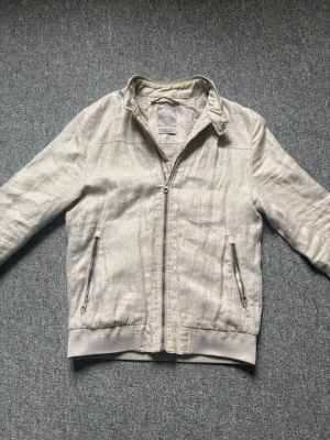 Ljusbeige tygjacka från Zara Man - Snygg ljusbeige tygjacka från Zara Man i lätt material. Jackan har dragkedja framtill, två fickor med dragkedja och ribbade muddar vid ärmslut och nederkant. Perfekt för vår och höst när du vill ha en stilren look.