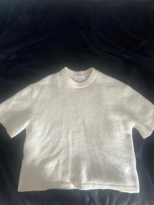 Vit stickad t-shirt Gina Tricot - Kortärmad stickad t-shirt i vit färg från Gina Tricot. Tillverkad i en mjuk ullblandning med ribbad halsringning och nederkant. Enkel och clean design som passar perfekt till jeans eller kjol.