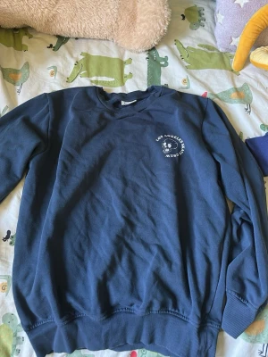 Blå sweatshirt med tryck - Cool blå sweatshirt med tryck på bröstet som är storlek 158-164cm och stort grafiskt tryck på ryggen med texten 'Los Angeles Skate Crew', skateboard, döskalle och milkshake. Tröjan har rund hals och ribbade muddar. Perfekt för dig som gillar streetwear och skatekultur.