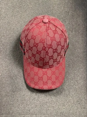 Rosa GG keps med GG-mönster - Säljer en rosa keps från GG med klassiskt GG-monogram i rött över hela kepsen. Kepsen har böjd skärm, justerbar rem bak och gröna/röda detaljer på sidorna. Materialet är canvasliknande tyg som känns både lyxigt och tåligt. Perfekt för dig som vill sticka ut.