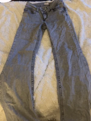 Gråa låg midjas jeans - Säljer ett par gråa jeans med utsvängda ben och klassisk femficksmodell. Jeansen har kontrastsömmar och coola broderade detaljer på bakfickorna. Tillverkade i denim med en avslappnad passform, perfekta till vardagslooken. Säljer pågrund av att dom är för små samt inte används.❤️