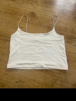Vit croppad linnetopp - Säljer en enkel och stilren vit croppad linnetopp med tunna axelband. Perfekt till sommaren och lätt att matcha med olika outfits. Tillverkad i mjuk bomull för en bekväm känsla.