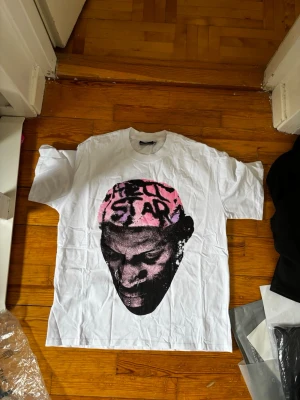 Vit Hellstar t-shirt med tryck - Säljer en vit t-shirt från Hellstar med stort grafiskt tryck i svart och rosa på framsidan och baksidan. Framsidan har ett ansikte med rosa text, baksidan har texten 'Hellstar Bad Boy' i graffiti-stil. Klassisk passform och korta ärmar. sitter våldigt stort