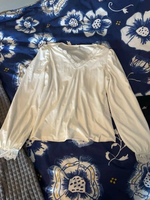 Vit blus med spetsdetaljer - Söt vit blus med långa ärmar och v-ringning. Blusen har fina spetsdetaljer både vid halsringningen och vid ärmsluten.