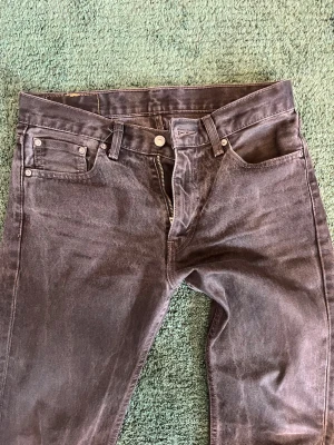 Svarta Levi's jeans 505 - Säljer ett par svarta jeans från Levi's med klassisk femficksdesign och rak passform. Jeansen har en snygg tvätt, dragkedja och knapp i midjan samt den ikoniska läderpatchen bak. Materialet är kraftig denim i bomull. Storlek 30/30