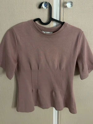 Ljusrosa figurnära t-shirt - Säljer en ljusrosa t-shirt med rund hals och korta ärmar. T-shirten har en figurnära passform och är tillverkad i mjuk bomull, perfekt för en enkel och stilren look.