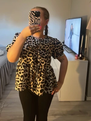 Leopardmönstrad blus med puffärm - Säljer en leopardmönstrad blus med puffiga korta ärmar och knytband framtill. Blusen har en lös passform och volangdetalj nedtill. Endast använd fåtal gånger 