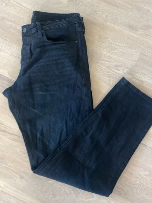 Svarta raka jeans Jack & Jones - Säljer ett par svarta jeans med rak passform och klassisk femficksdesign. Jeansen har normal midja och stängs med knapp och dragkedja. Materialet är denim med en lätt stretch för extra komfort. Modell Mike. Stl 36x34