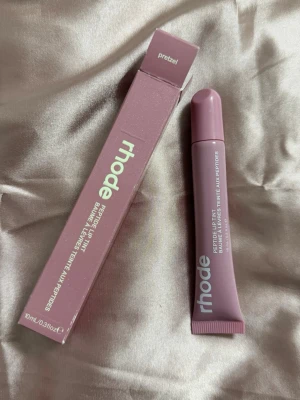 rhode Peptide Lip Tint Pretzel - Peptide Lip Tint från rhode i färgen Pretzel. Läppbalsamet kommer i en mjuk tub med skruvkork och har en snygg rosa-brun nyans. Förpackningen är stilren och modern med vit text. Innehåller 10 ml.