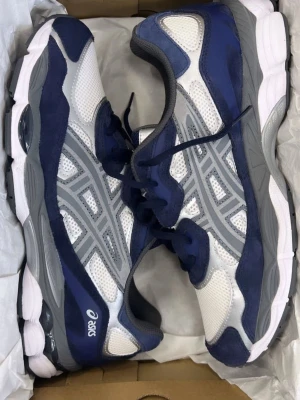 Asics Gel Nyc - vit/mörkblå - Snygga sneakers från Asics i blått, vitt och grått. Skorna har meshpaneler för bra ventilation, klassiska Asics-stripes på sidorna och en chunky sula för skön komfort. Skickar inom 1 dag, pris kan alltid diskuteras. Box medföljer 