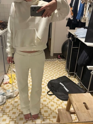Beige loungewear set med hoodie - Mysigt loungewear set i ljus gul med en oversized hoodie och matchande byxor med resår i midjan. Hoodien har stor ficka framtill och ribbade muddar. Perfekt för chill dagar hemma eller när du vill vara bekväm men ändå snygg. Bandet har åkt ur men det går att fixa enkelt när man får hem varan! DEN ÄR LJUS GUL INTE VIT lite mer gul i verkligheten. Skriv om du har en fråga. Huddin är xxs men på byxorna står det ingen storlek men passar mig som är 164 cm.