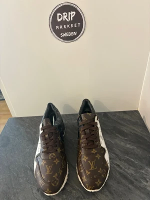 bruna läder skor  - Snygga sneakers i brunt med klassiskt monogrammönster i storlek 45 i guld. Skorna har vita detaljer på sidorna och svart hälparti. Tillverkade i läder med bruna skosnören och vit sula. Perfekta för dig som vill sticka ut med exklusiv stil.