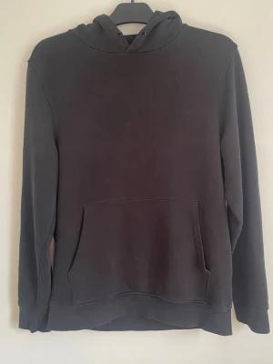 Dressmann hoodie  - En stilren svart hoodie med huva och dragsnören. Hoodien har en klassisk magficka och långa ärmar. Perfekt för en avslappnad look. Materialet känns mjukt och bekvämt mot huden.