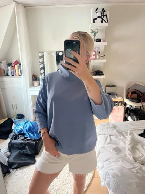 Ljusblå oversized polotröja - Säljer en ljusblå oversized polotröja med trekvartsärmar och hög krage. Tröjan har en avslappnad passform och är gjord i ett mjukt, bekvämt material som passar perfekt för en chill och stilren look.