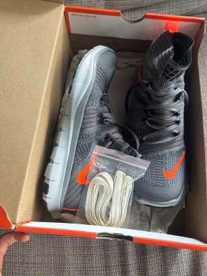 Limited edition Gråa Nike high-top skor - Snygga gråa high-top sneakers/ joggingskor från Nike med stickad ovandel och orange swoosh på sidan. Skorna har en flexibel vit sula och kommer med extra vita skosnören. Perfekt för dig som vill ha en sportig och modern look. skorna är inspirerade av Andrés Iniesta genom att de följer samma principer som Nike använde när de designade skor för hans spelstil: flexibilitet, låg vikt och naturlig rörelse. Modellen är från 2013. Aldrig använt!  
