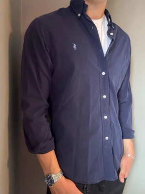 Ralph Lauren skjorta marinblå – M slim fit - Säljer denna stilrena och snygga blåa Ralph Lauren skjortan. Skjortan är i mycket bra skick förutom lite missfärgningar se sista bilderna. Skjortan passar perfekt för både vardag och mer uppklädda tillfällen. Storlek M slim fit. Har du några frågor? Tveka inte att höra av dig. Allt gott från Deluxe Garderoben 