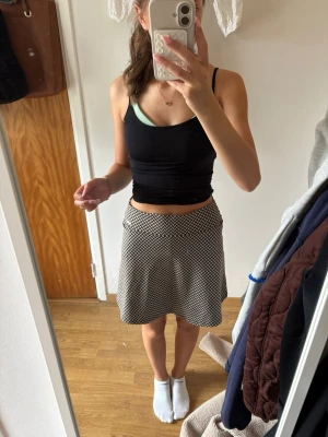 Tennis kjol med shorts - Säljer en svartbege kortkjol med rutigt mönster och inbyggda shorts under. Kjolen har en A-linjeformad passform och är gjord i ett mjukt, stretchigt material som känns bekvämt. Perfekt för dig som vill ha både stil och rörelsefrihet.