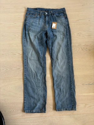  Levi's Jeans ( Budgivning)  - Klassiska blå jeans från Levi's med rak passform och fem fickor. Jeansen har en snygg tvättad look och orangea sömmar. Tillverkade i slitstarkt denimtyg, perfekta för en avslappnad stil.