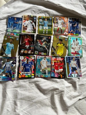 Samling av fotbollsspelkort, 15 st och nästan alla är från England  - Säljer en samling med olika fotbollsspelkort från Panini och Topps, med spelare från Premier League och internationella lag. Korten har färgstarka designer, holografiska effekter och visar spelare i matchställ. Perfekt för dig som gillar att samla på fotbollskort eller vill byta med vänner.