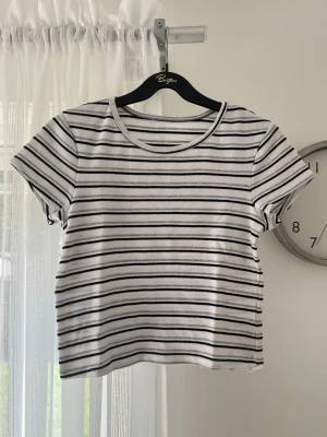 Randig croppad t-shirt - En croppad t-shirt med svarta, vita och gråa ränder. Köpt second hand en gång i tiden men blev använd ca 2 gånger. Väldigt stretchigt och skönt material.  Vet ej exakt storlek, men uppskattar den till en S.