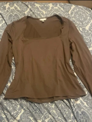 Brun långärmad topp från H&M - Brun långärmad topp från H&M med fyrkantig ringning. tillverkad i ett mjukt och stretchigt material som känns bekvämt mot huden. Perfekt att styla med jeans eller kjol för en trendig look.