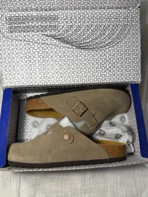 Taupe Birkenstock Boston 38 - Säljer ett par beige Birkenstock Boston sandaler i mocka med justerbart spänne i metall. Sandalerna har en klassisk täckt tå och korksula för extra komfort. Perfekta för en avslappnad och trendig stil. ‼️Skickar inom 24H‼️ **PRIS KAN DISKUTERAS**