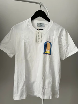 Vit t-shirt från Casablanca - Vit t-shirt från Casablanca med tryck i blått, gult och orange på bröstet. Klassisk rund hals och korta ärmar. Prislappen är på den är helt ny, PRISET GÅR ATT DISKUTERA VID SNABB AFFÄR 
