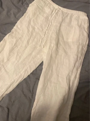 Vita linnebyxor med dragsko - Säljer ett par vita linnebyxor med avslappnad passform och elastisk midja med dragsko. Byxorna är tillverkade i svalt linnematerial och har raka ben. Perfekta för en chill och stilren look. Andvända få gånger så i bra skick