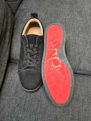 Christian louboutin - Snygga svarta christian louboutin med ovandel i mocka och klassisk snörning. Skorna har en ikonisk röd sula med mönster och svart kant. Insidan är beige och skon har en låg profil som passar till många olika stilar. Dom har små tecken på användning så som under sulan, Dom ska användas så kommer inte märkas så mycket. 