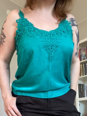 Grönblått linne - Teal-ish linne från Cream i strl 38/M-L med spetsdetaljer längs kragen. Thriftat, i toppenskick. Läs gärna bion innan köp. 