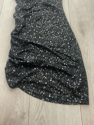 Svart långkjol med vita prickar - Svart långkjol med vita prickar i ett coolt mönster. Kjolen har en lätt böljande form och är gjord i ett mjukt, följsamt material som känns skönt mot huden. Perfekt för dig som vill ha en unik och trendig look.
