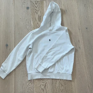 Vit hoodie från Polo Ralph Lauren - Vit hoodie från Polo Ralph Lauren med klassisk broderad logga på bröstet. Tröjan har huva, lång ärm och en stor magficka framtill. Tillverkad i mjuk bomull som är skön mot huden🤩Hör gärna av er vid funderingar😅